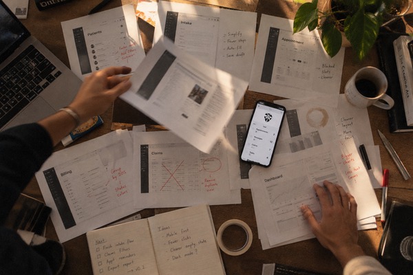 Printed screen layouts spread across a desk, one being lifted